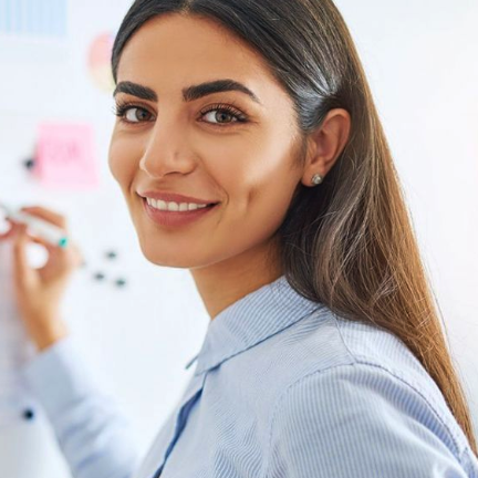 A photo of a teacher smiling and looking at the camera while writing on a whiteboard.